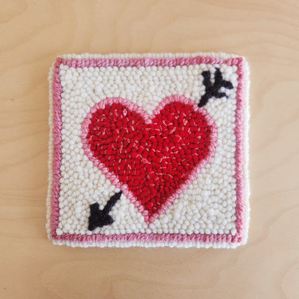red and pink punch needle heart with an arrow through it on a white background