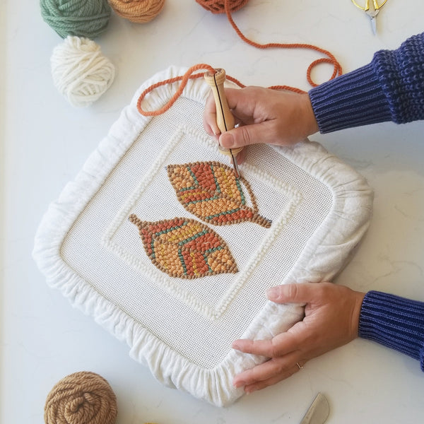 above the table shot of two hands in progress punching a design of two leaves stretched on backing fabric