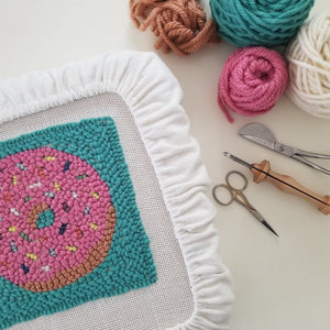 punched donut pattern still stretched on the frame with yarn and punch needle tools nearby