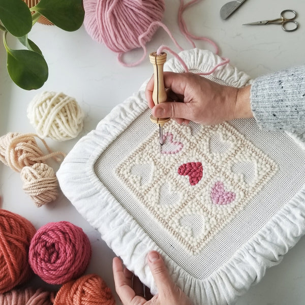 hands punching heart shaped design on monkscloth using an oxford punch needle
